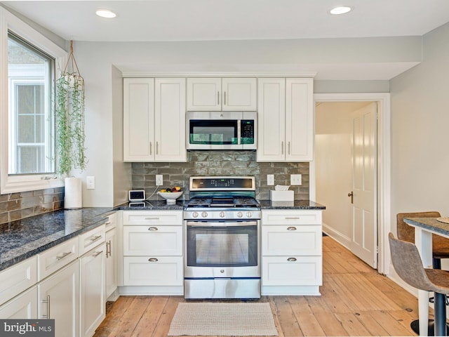 kitchen featuring dark stone counters, stainless steel appliances, white cabinetry, and tasteful backsplash