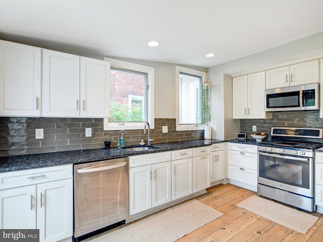 kitchen with dark stone counters, white cabinets, a sink, light wood finished floors, and stainless steel appliances