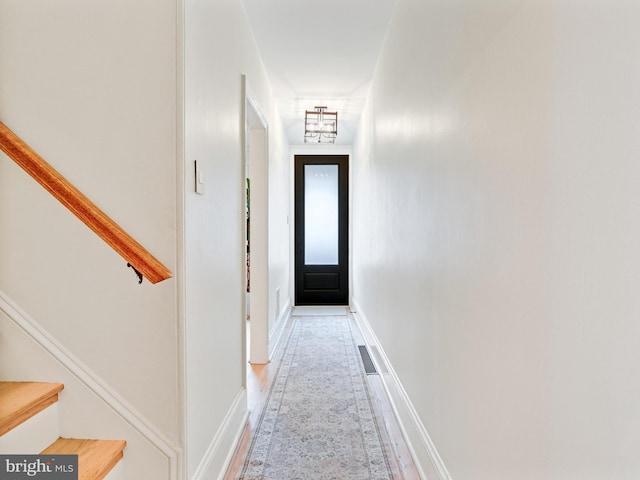 hall with light wood-type flooring, stairs, baseboards, and visible vents