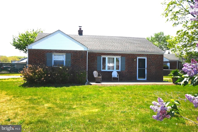 rear view of house with a patio, brick siding, a chimney, and a lawn
