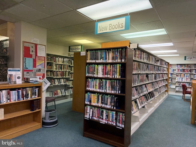 miscellaneous room featuring wall of books, a paneled ceiling, and carpet floors