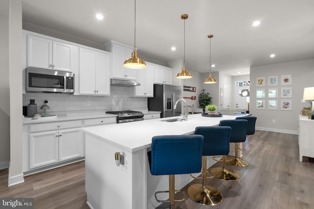 kitchen featuring wood finished floors, a center island with sink, light countertops, tasteful backsplash, and stainless steel appliances