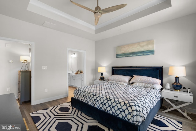 bedroom featuring connected bathroom, baseboards, wood finished floors, and a raised ceiling