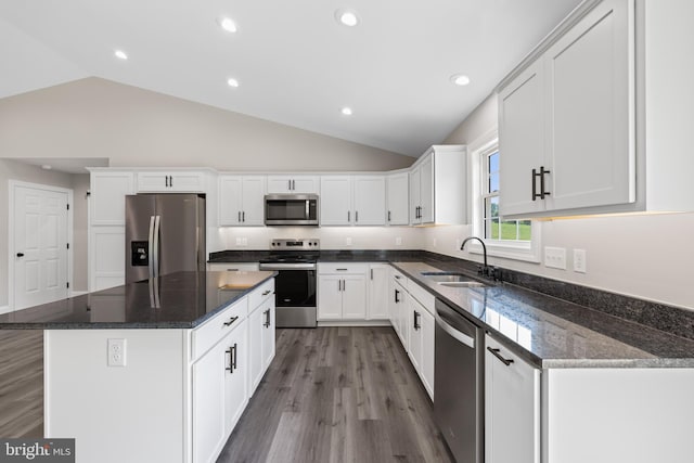 kitchen with white cabinetry, a sink, appliances with stainless steel finishes, a center island, and vaulted ceiling