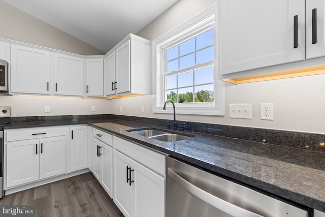 kitchen with dark stone counters, white cabinets, a sink, dishwasher, and vaulted ceiling