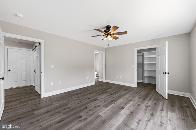 unfurnished bedroom with baseboards, a spacious closet, and wood finished floors