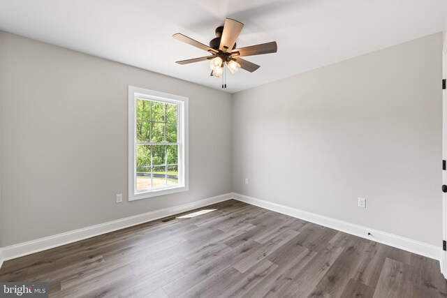 empty room with wood finished floors, a ceiling fan, and baseboards