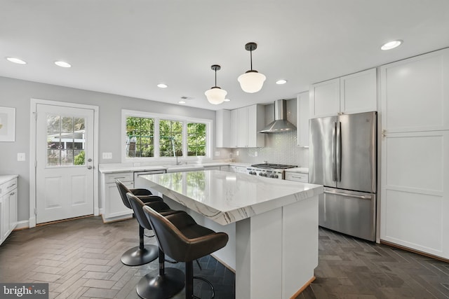 kitchen featuring wall chimney range hood, a sink, a kitchen island, freestanding refrigerator, and stove