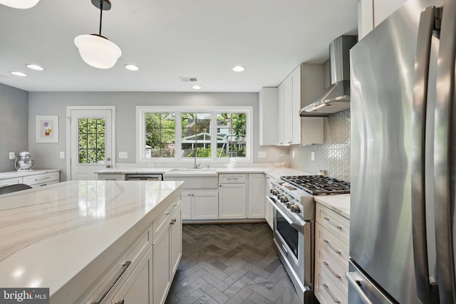 kitchen featuring light stone counters, stainless steel appliances, wall chimney range hood, a sink, and visible vents