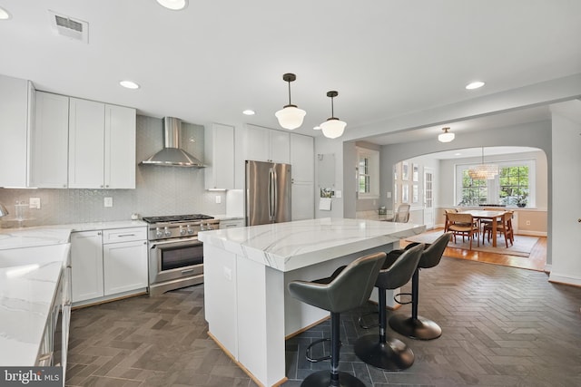 kitchen with arched walkways, light stone counters, stainless steel appliances, wall chimney range hood, and visible vents