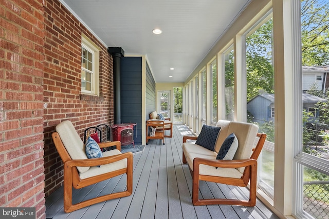 sunroom with a wood stove, an outdoor hangout area, hardwood / wood-style flooring, and brick wall