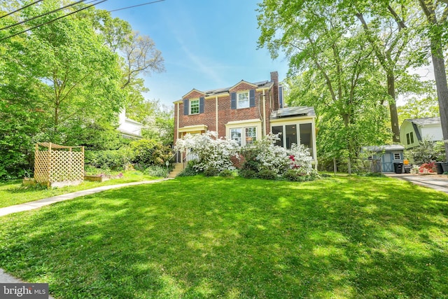 view of front facade featuring a chimney, a front yard, solar panels, brick siding, and a sunroom