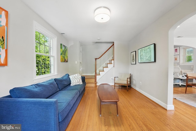 living room with a wealth of natural light, light wood-style floors, baseboards, and arched walkways