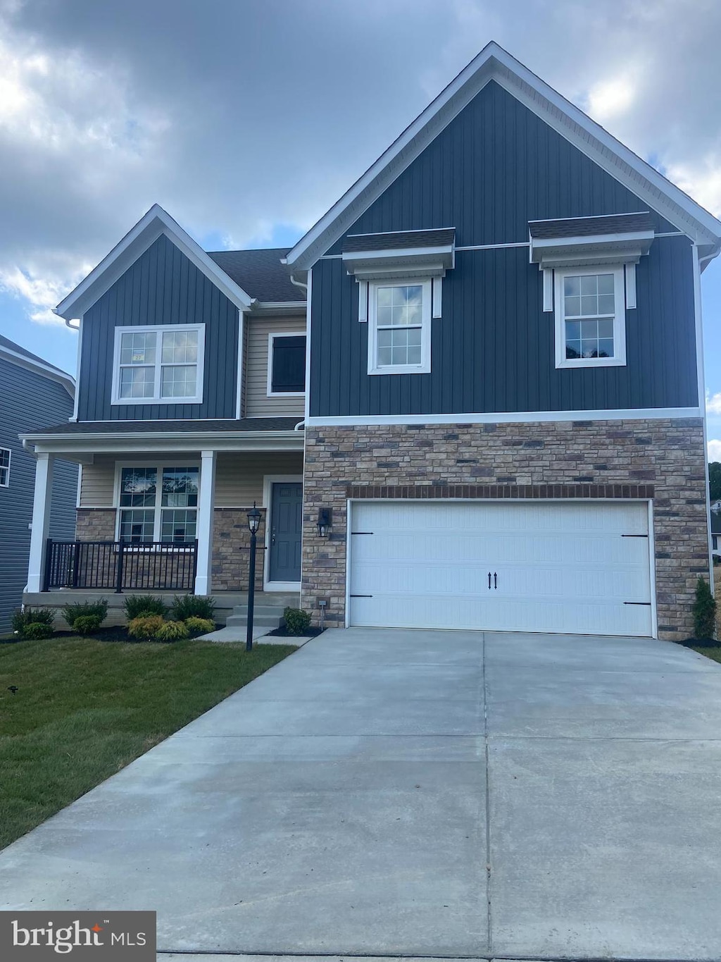 craftsman inspired home with driveway, stone siding, covered porch, an attached garage, and a front lawn