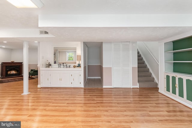 4 Hallbrook Ct, Baltimore, MD 21236 - unfurnished living room with a warm lit fireplace, light wood finished floors, baseboards, visible vents, and stairway