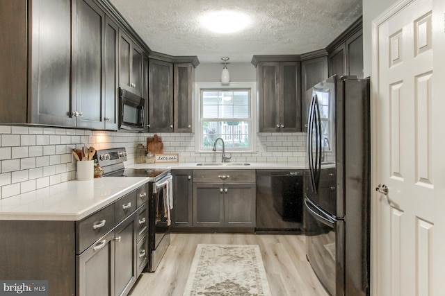 kitchen with light wood finished floors, a sink, black appliances, backsplash, and a textured ceiling