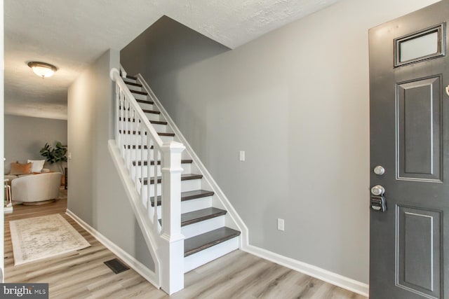 stairs with a textured ceiling, wood finished floors, visible vents, and baseboards