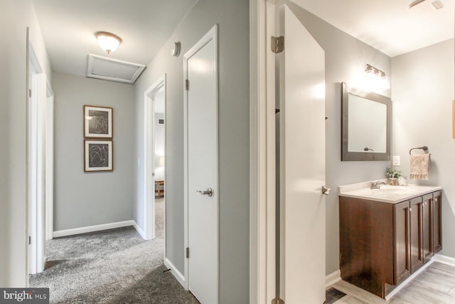 hallway with attic access, light colored carpet, baseboards, and a sink