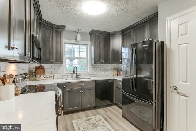 kitchen with light wood-style floors, black appliances, backsplash, a sink, and a textured ceiling