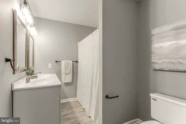 full bath featuring double vanity, a sink, toilet, and baseboards