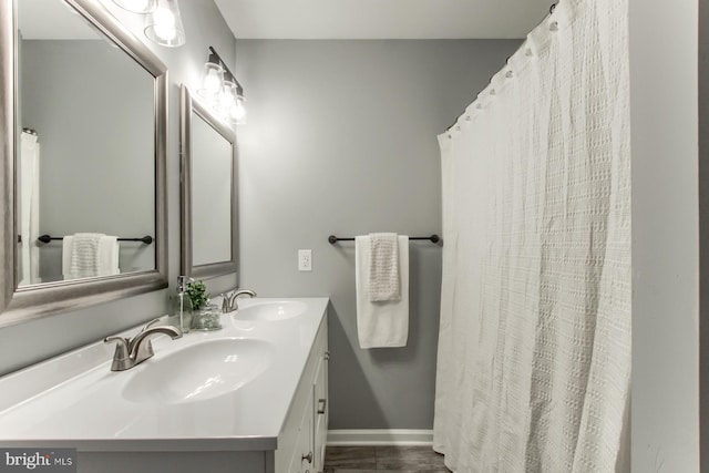 bathroom featuring baseboards, double vanity, and a sink