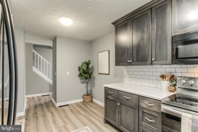 kitchen featuring black appliances, light countertops, light wood finished floors, and backsplash
