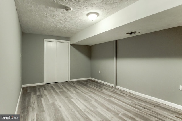 finished basement featuring wood finished floors, visible vents, baseboards, and a textured ceiling