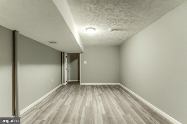 finished basement featuring a textured ceiling, light wood-style floors, visible vents, and baseboards
