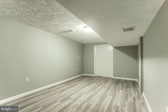 finished basement with baseboards, visible vents, wood finished floors, and a textured ceiling