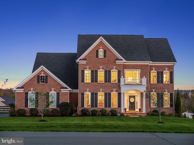 georgian-style home featuring brick siding, a lawn, and roof with shingles