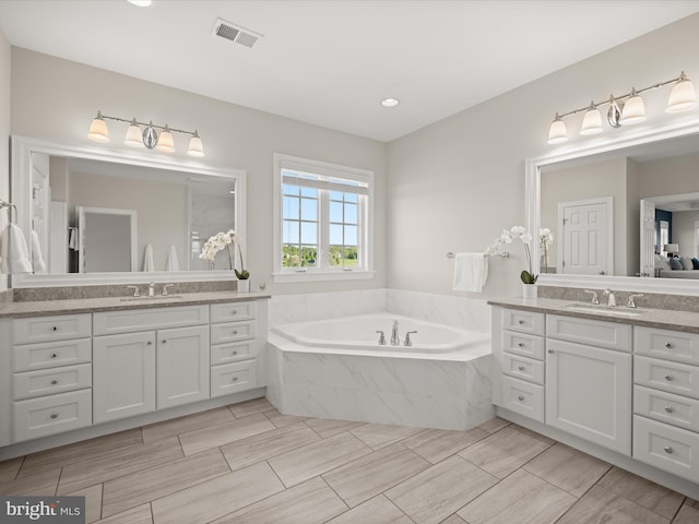 bathroom with visible vents, a sink, a bath, and two vanities