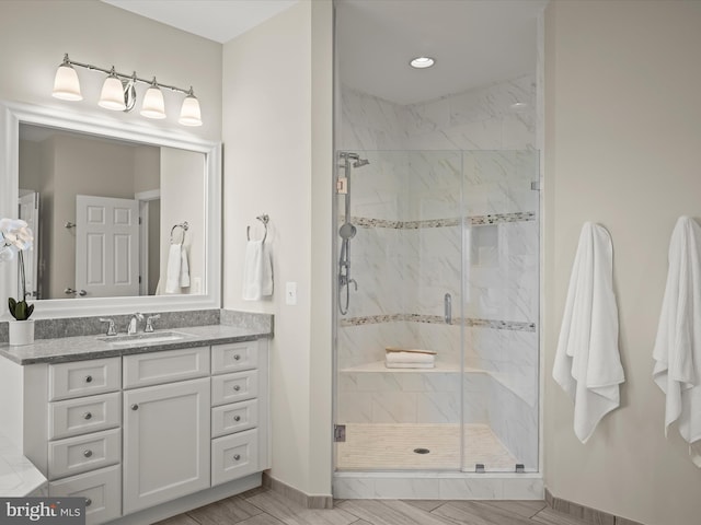 full bath with baseboards, a marble finish shower, and vanity