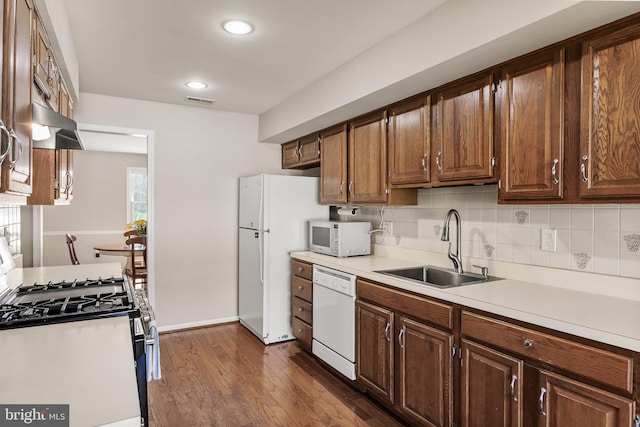 kitchen with a sink, decorative backsplash, under cabinet range hood, white appliances, and light countertops