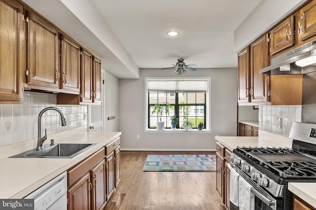 kitchen with stainless steel gas range, light countertops, under cabinet range hood, and a sink