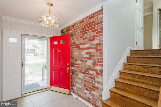 entrance foyer featuring an inviting chandelier, ornamental molding, and brick wall