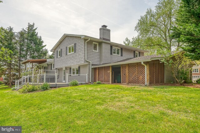 rear view of house with a lawn, brick siding, a chimney, and a wooden deck