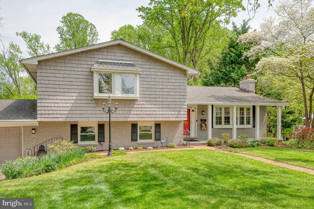 split level home featuring a garage, a front yard, roof with shingles, a chimney, and brick siding
