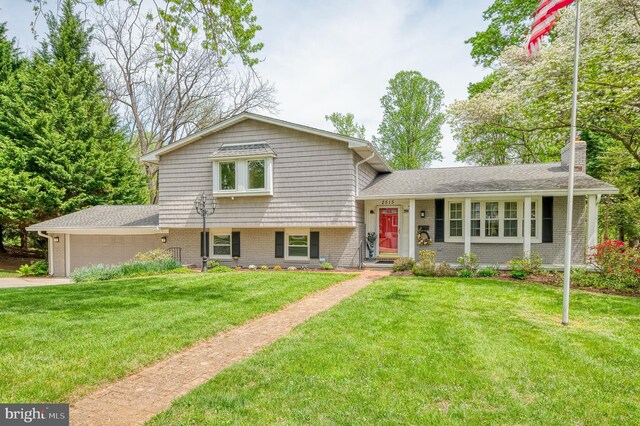 split level home with an attached garage, a front lawn, brick siding, a chimney, and driveway
