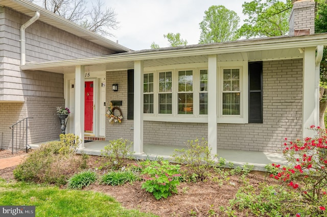 entrance to property with brick siding, covered porch, and a chimney