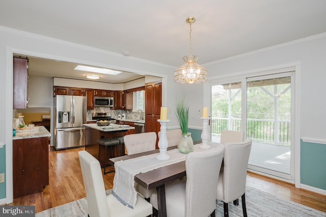 dining area with an inviting chandelier, ornamental molding, light wood finished floors, and baseboards