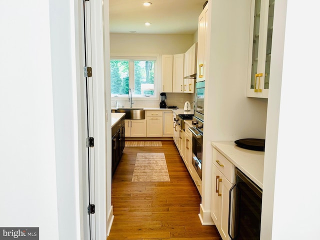 kitchen with wood finished floors, decorative backsplash, a sink, white cabinetry, and wine cooler