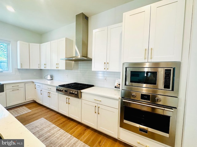 kitchen featuring stainless steel appliances, light countertops, light wood-style flooring, and wall chimney exhaust hood