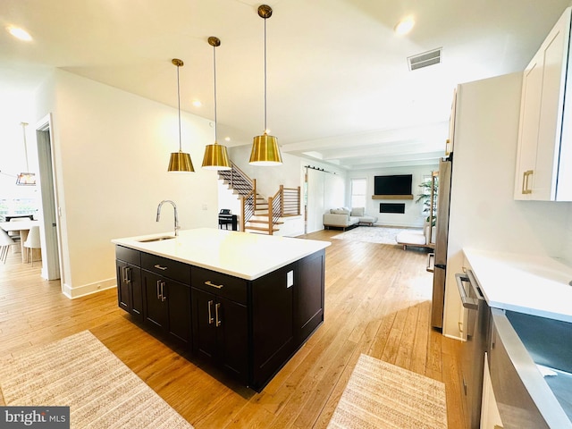 kitchen with a sink, light wood-style floors, dark cabinets, and visible vents