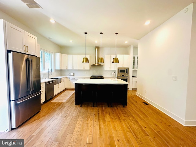 kitchen featuring a sink, wall chimney exhaust hood, light wood-style flooring, light countertops, and appliances with stainless steel finishes
