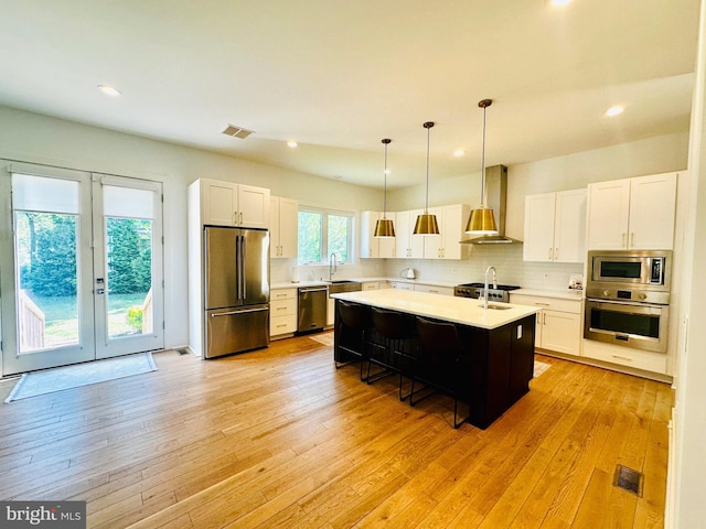 kitchen featuring a sink, wall chimney exhaust hood, visible vents, light countertops, and appliances with stainless steel finishes