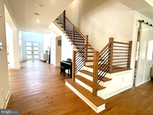 stairs with a barn door, french doors, baseboards, and wood-type flooring