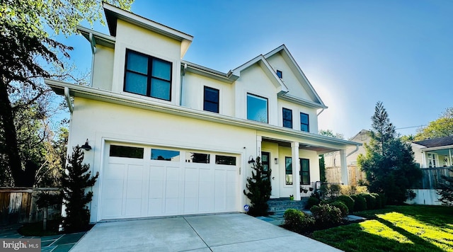 modern farmhouse style home with a front lawn, a garage, covered porch, stucco siding, and fence