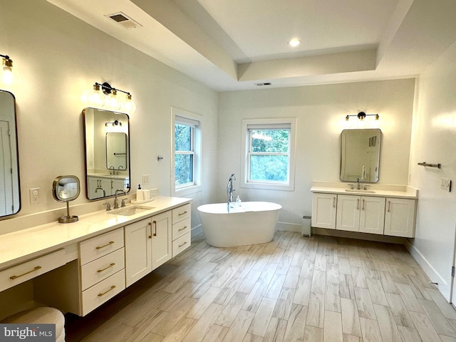 bathroom featuring a sink, a freestanding tub, a raised ceiling, visible vents, and wood finished floors