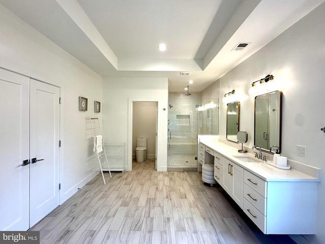 bathroom featuring wood finished floors, toilet, vanity, visible vents, and a stall shower