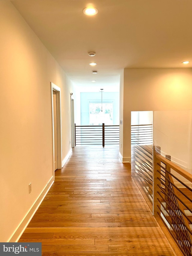 hall featuring baseboards, light wood-type flooring, an upstairs landing, and recessed lighting